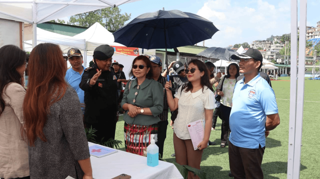 Group of women including Minister Pi Lalrinpuii and young participants standing together under a black umbrella.