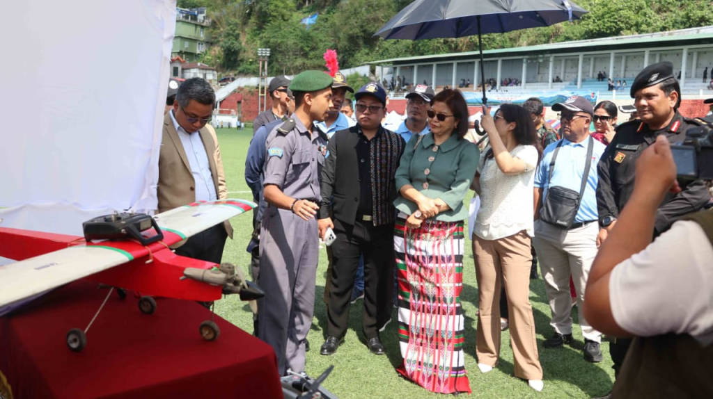 Minister Pi Lalrinpuii interacting with officials and a woman in traditional Mizo puan while walking through the venue.